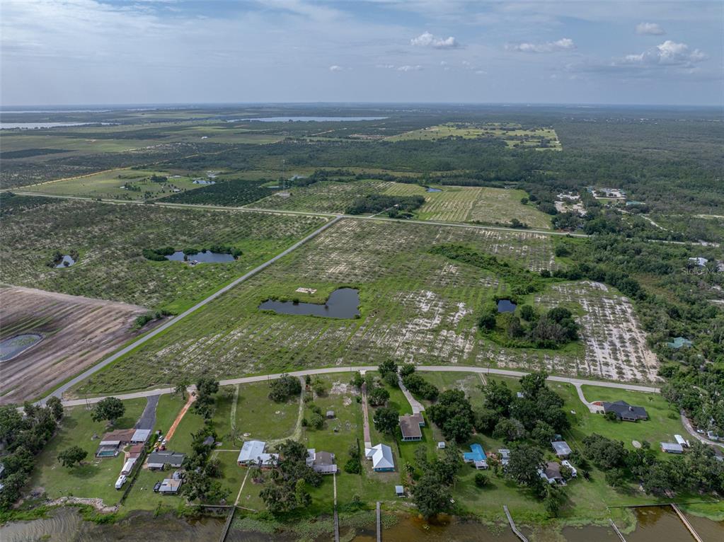 An aerial view shows a residential neighborhood along a lakefront with large, undeveloped grassy fields — 0 LAKE REEDY BOULEVARD, FROSTPROOF, FL