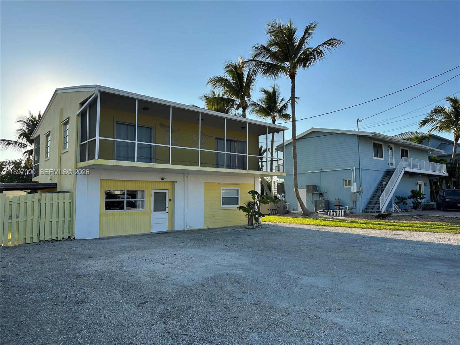 A two-story yellow house with a screened-in balcony stands next to a blue house — 164 Venetian Dr, Islamorada FL 33036, ISLAMORADA, FL