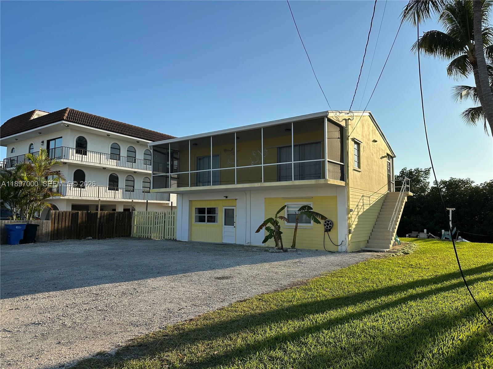 A two-story yellow house features a screened-in upper balcony and an external staircase — 164 Venetian Dr, Islamorada FL 33036, ISLAMORADA, FL