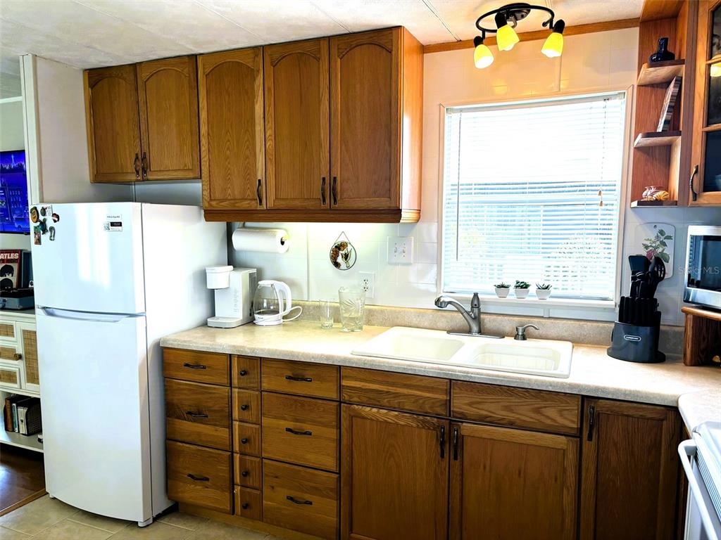 A kitchen features oak cabinets, a white refrigerator, a double sink, and a window — 6444 HAELE COURT, NORTH PORT, FL