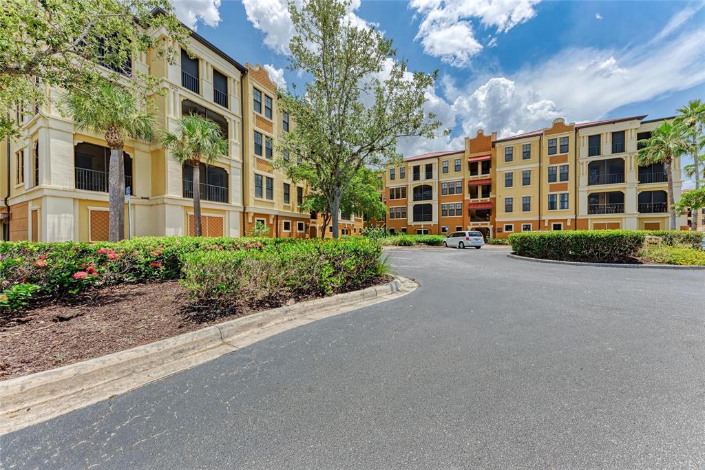 A paved driveway leads toward multi-story apartment buildings surrounded by landscaping and palm trees — 96 VIVANTE BOULEVARD UNIT 210, PUNTA GORDA, FL