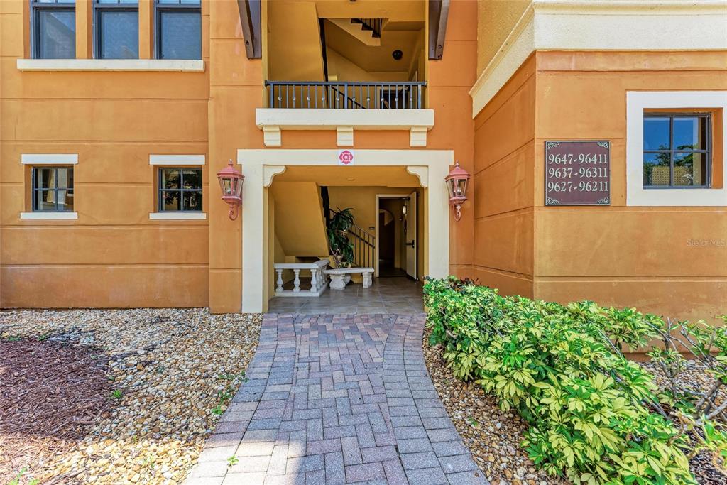 A paved walkway leads to the entrance of a tan stucco apartment building — 96 VIVANTE BOULEVARD UNIT 210, PUNTA GORDA, FL