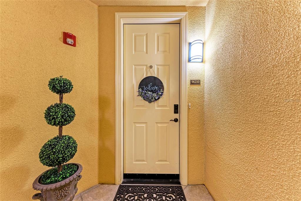 A front door with a welcome wreath is flanked by a topiary and wall light — 96 VIVANTE BOULEVARD UNIT 210, PUNTA GORDA, FL