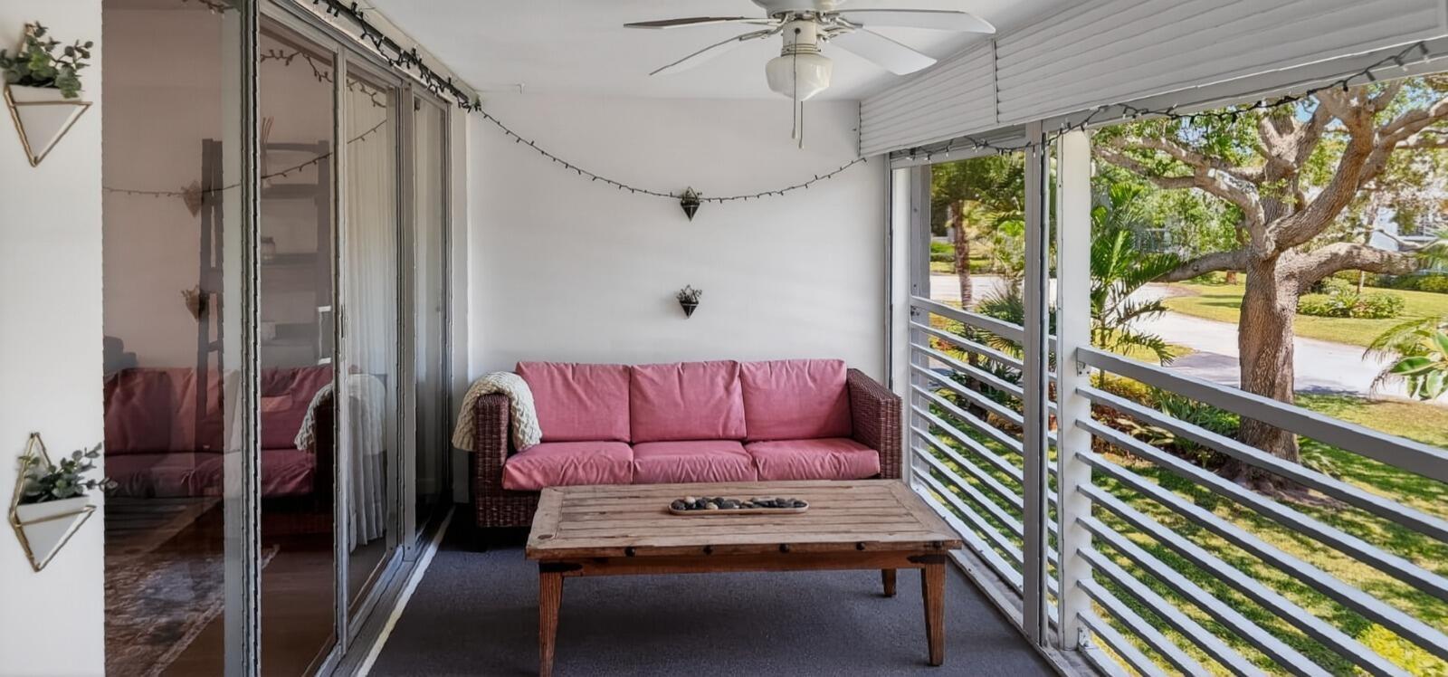A screened-in porch features a pink wicker sofa, wooden coffee table, and ceiling fan — 8 Garden Street # 206r, Tequesta FL 33469, TEQUESTA, FL