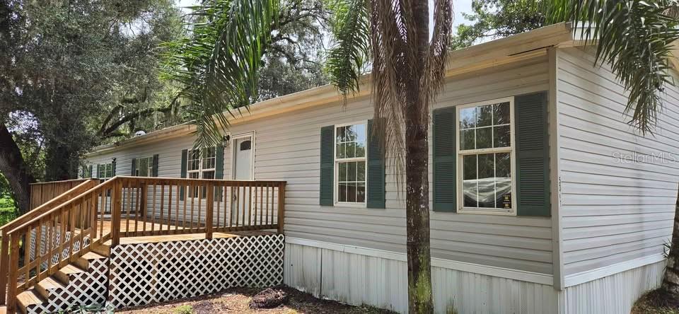 A light-colored mobile home features a wooden deck with stairs and green window shutters — 5301 ROYAL OAK DRIVE, TAMPA, FL