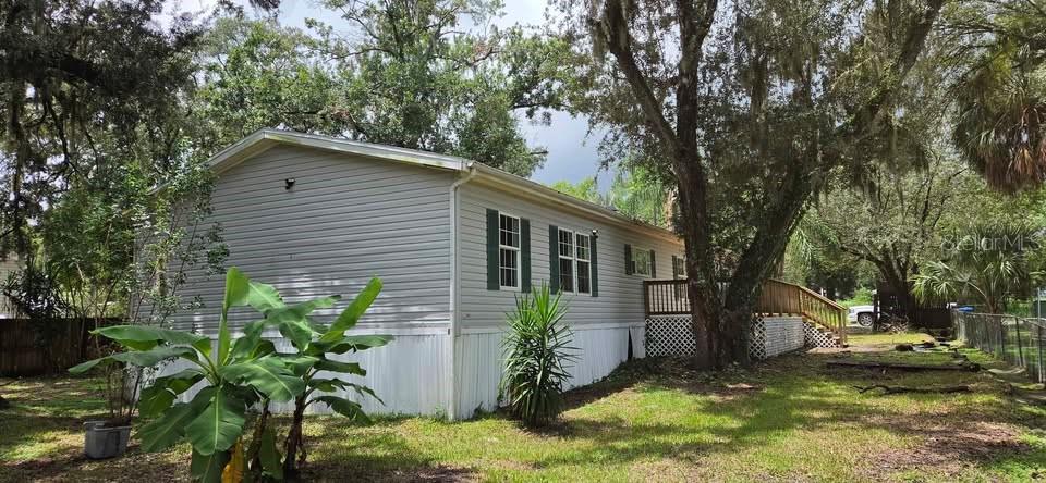 A light gray mobile home with a wooden deck stands in a grassy, tree-filled yard — 5301 ROYAL OAK DRIVE, TAMPA, FL
