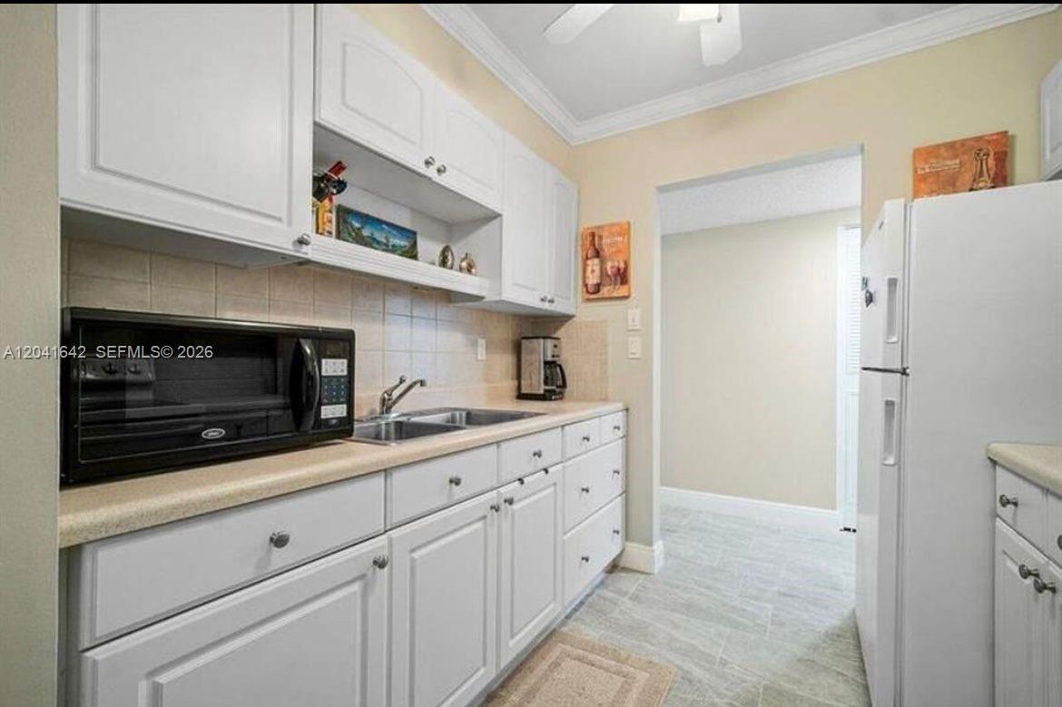 A kitchen features white cabinets, a black microwave, a stainless steel sink, and tile flooring — 250 NE 20th St # 3030, Boca Raton FL 33431, BOCA RATON, FL