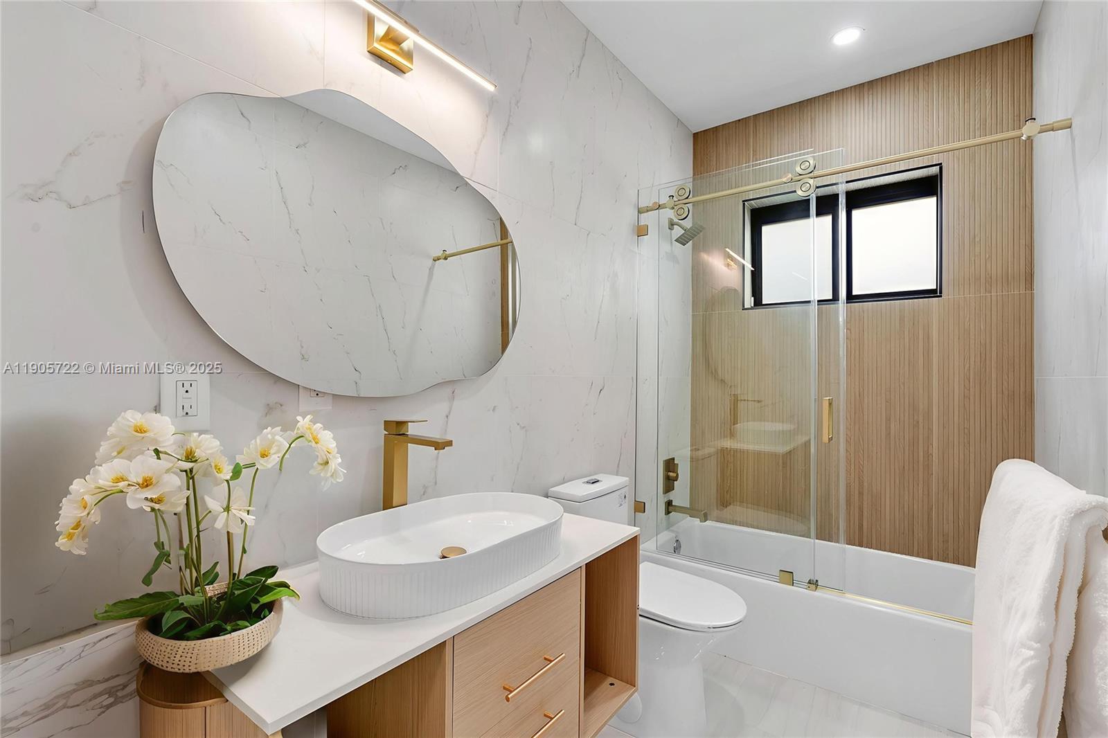A modern bathroom features a marble-tiled wall, a wood vanity, and a glass-enclosed bathtub — 8635 N Miami Ave, Miami FL 33150, MIAMI, FL