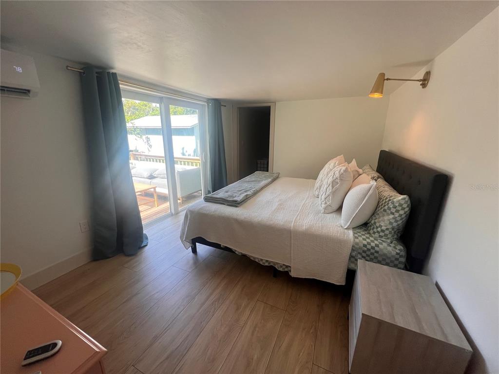 A bedroom features wood-look flooring, a dark headboard, and a sliding glass door to a deck — 2921 WILSON AVENUE, PUNTA GORDA, FL
