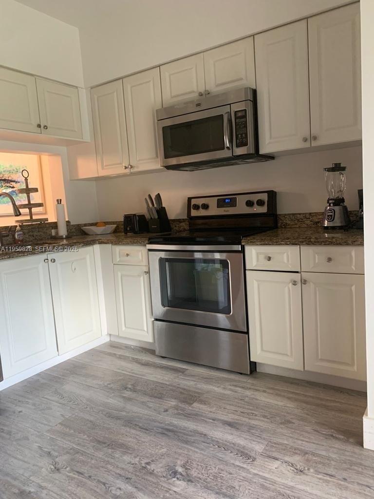 A kitchen features white cabinets, stainless steel appliances, and granite countertops over wood-look flooring — 20 Key West Ct, Weston FL 33326, WESTON, FL