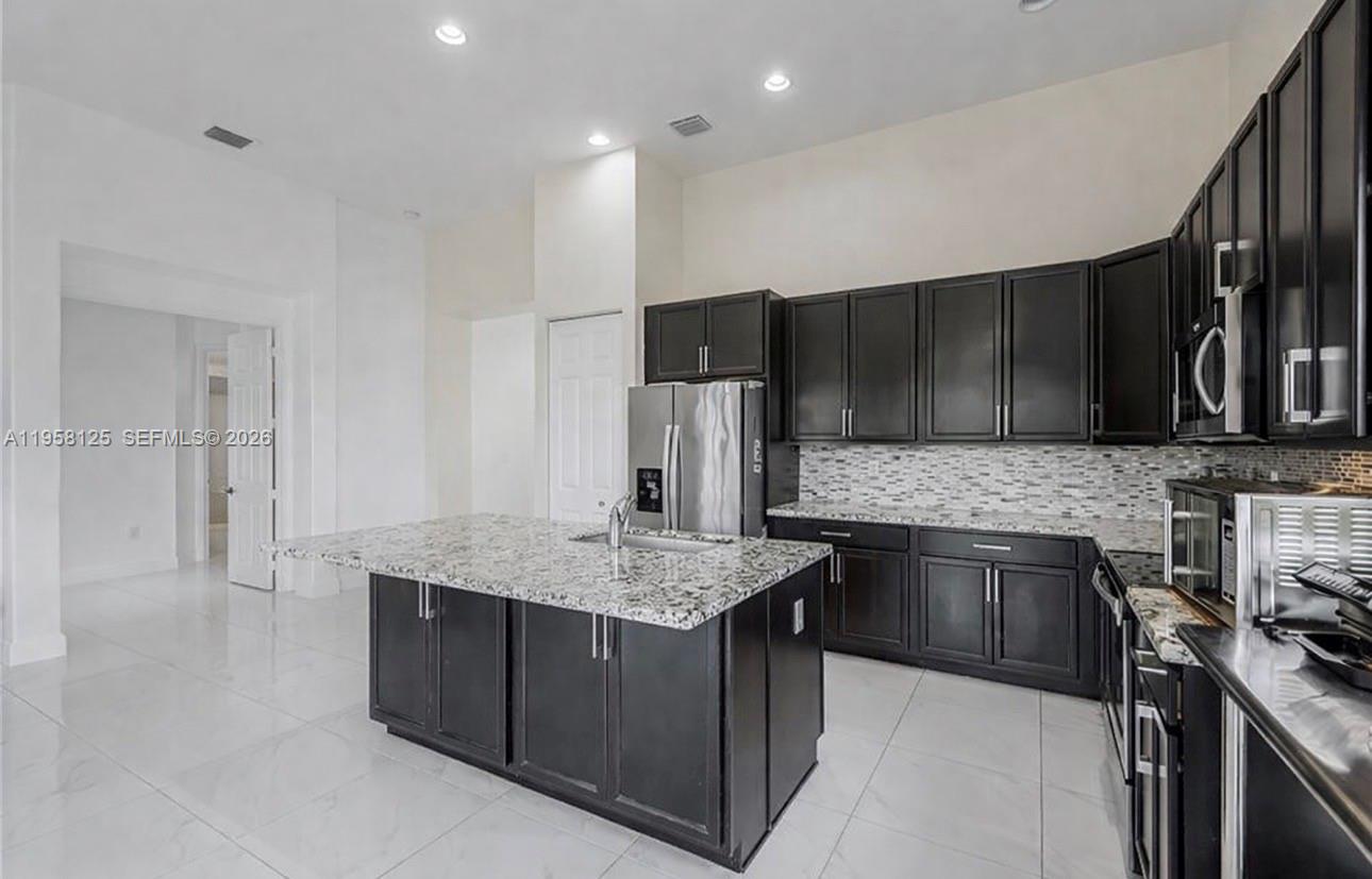 A kitchen features dark cabinetry, granite countertops, a central island, and white tile flooring — 4761 ROSETTA TER, Ave Maria FL 34142, AVE MARIA, FL