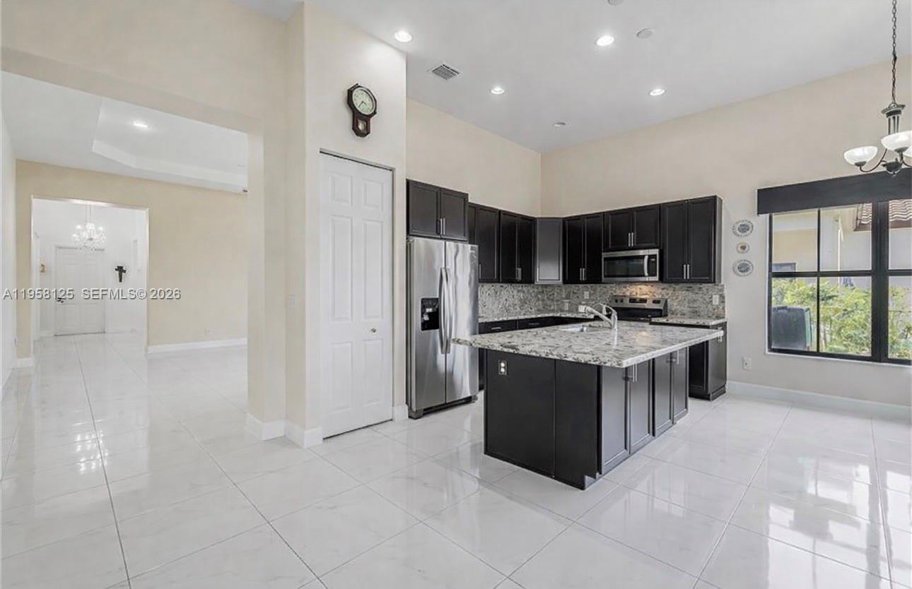 A kitchen features dark cabinets, a granite island, and white tile flooring — 4761 ROSETTA TER, Ave Maria FL 34142, AVE MARIA, FL