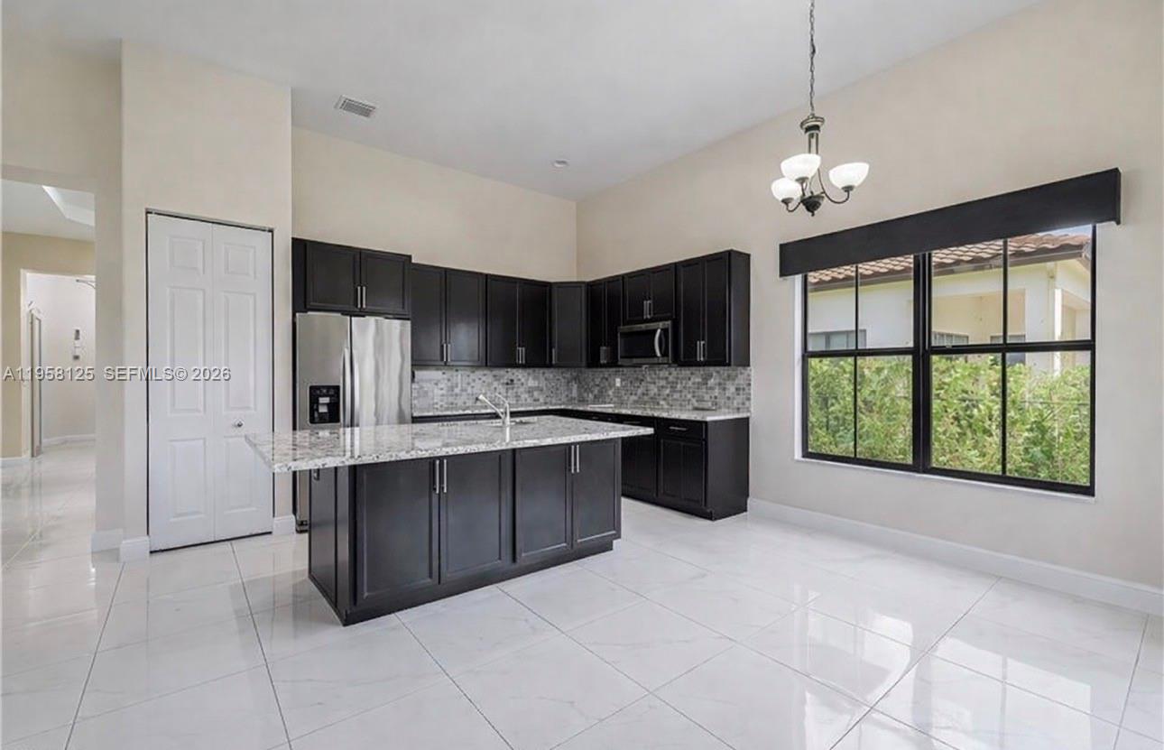 A kitchen features dark cabinetry, granite countertops, a center island, and white tile flooring — 4761 ROSETTA TER, Ave Maria FL 34142, AVE MARIA, FL
