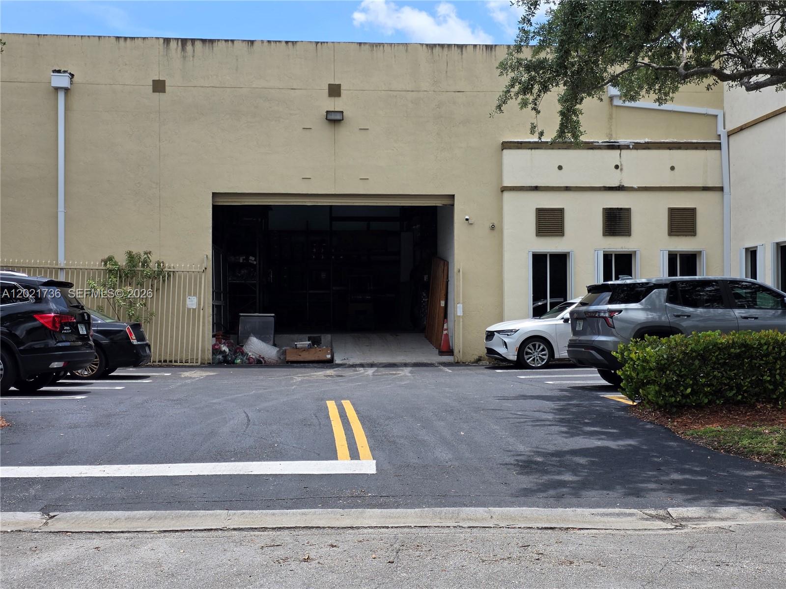 The exterior of a commercial warehouse building features a large open bay door and parking — 10420 NW 37th Ter, Doral FL 33178, DORAL, FL