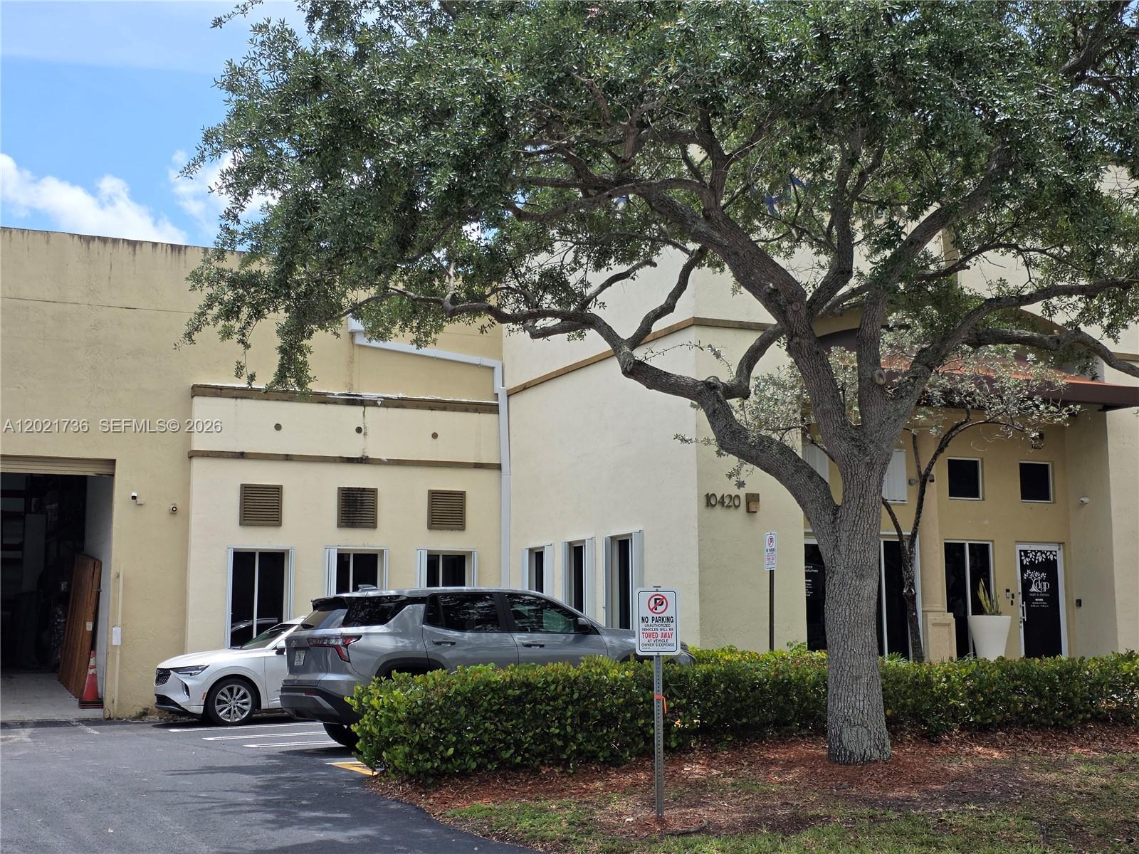 A tan commercial building exterior features a large tree, parking spaces, and a no-parking sign — 10420 NW 37th Ter, Doral FL 33178, DORAL, FL