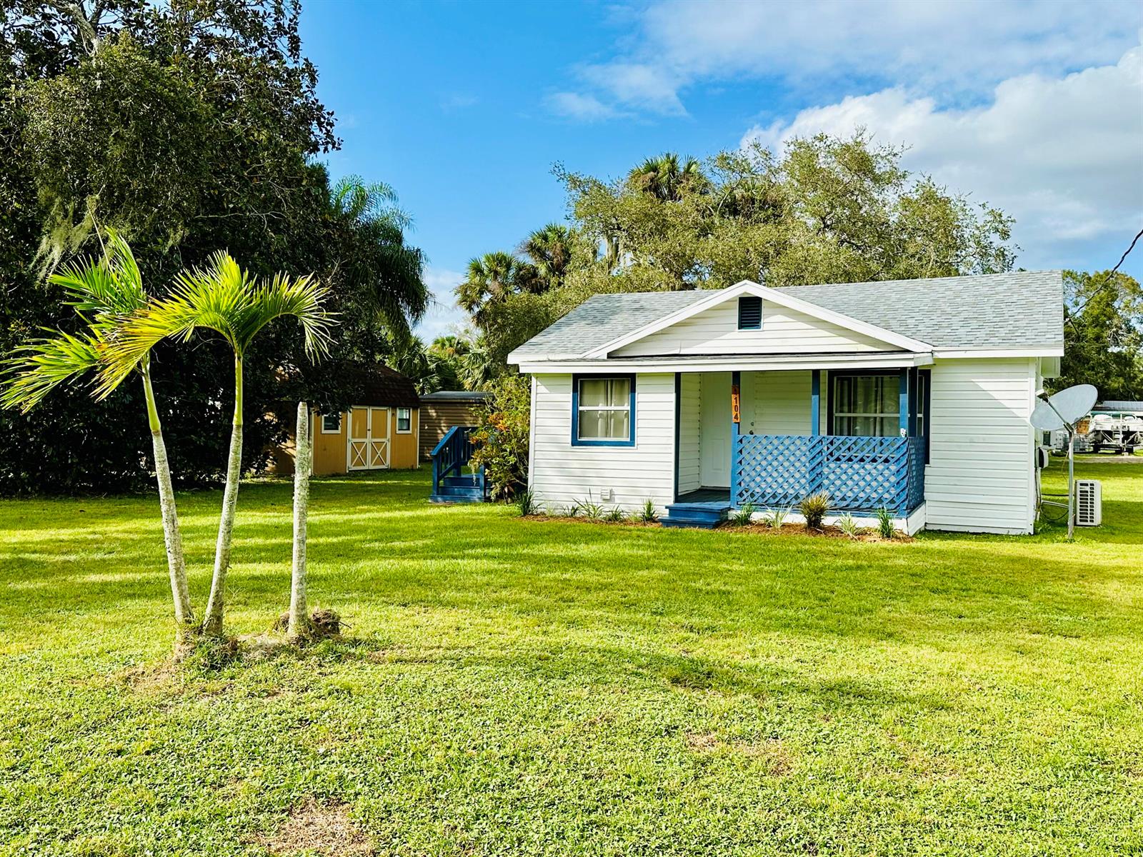 A white cottage with a blue lattice porch sits on a grassy lot with palm trees — 1104 SW 11th Street, Okeechobee FL 34974, OKEECHOBEE, FL