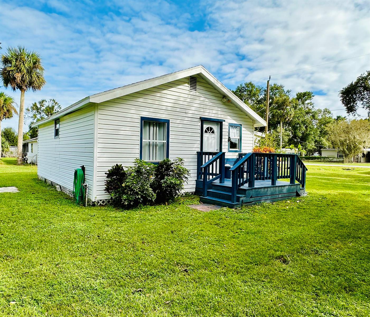 A small white house with blue trim and a front deck sits on a grassy lawn — 1104 SW 11th Street, Okeechobee FL 34974, OKEECHOBEE, FL