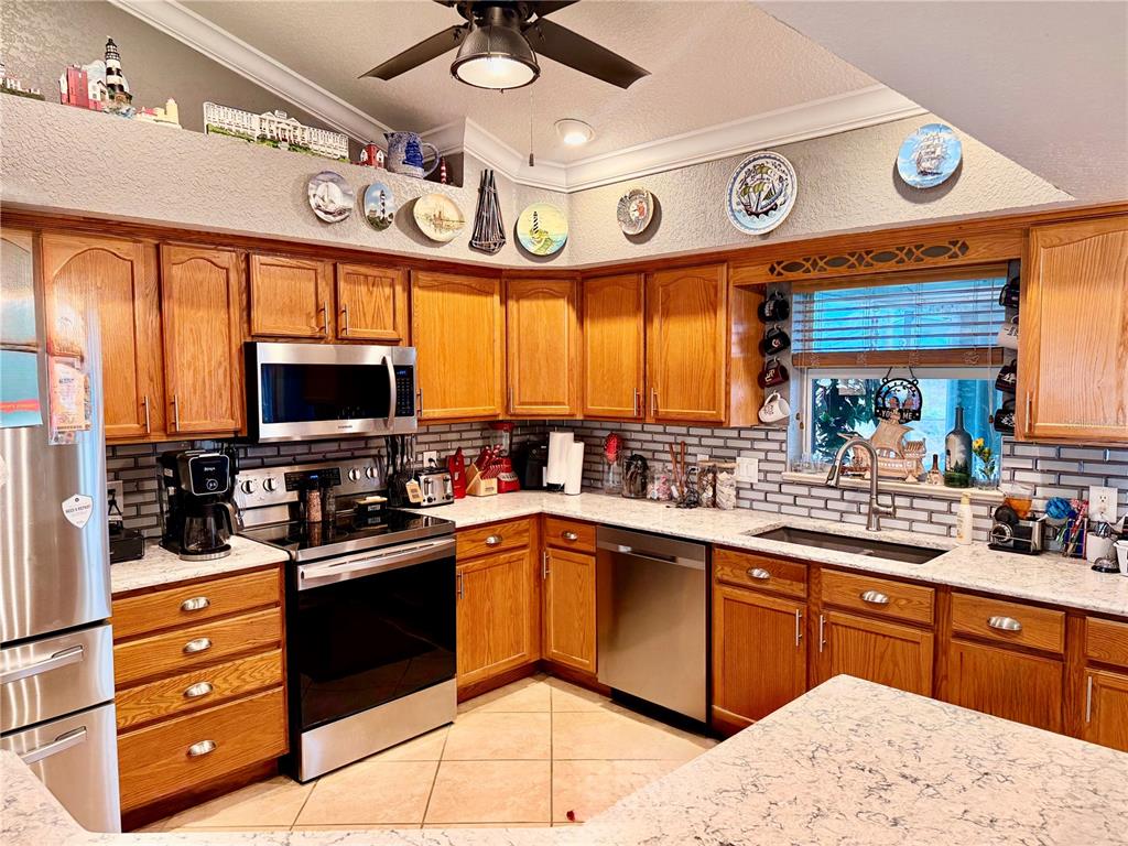 A kitchen features oak cabinets, stainless steel appliances, and light-colored countertops with a tiled backsplash — 478 HUMPHREY AVENUE, LAKE PLACID, FL