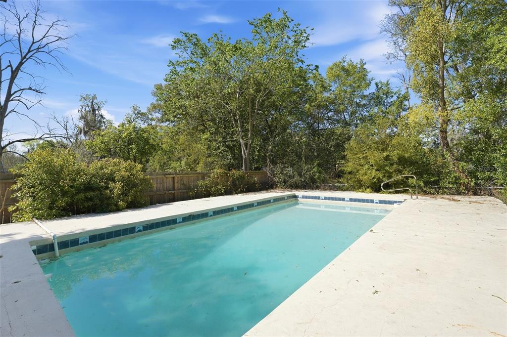 An outdoor rectangular swimming pool with a concrete deck surrounded by trees and a fence — 1324 PLACID PLACE, JACKSONVILLE, FL