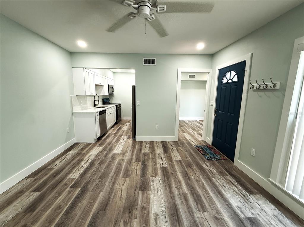 A kitchen with white cabinets and wood-look flooring opens into a living area with a door — 201 MEDALLION BOULEVARD UNIT D, MADEIRA BEACH, FL