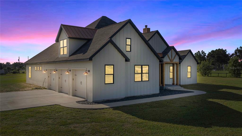 A white farmhouse-style home with a three-car garage and a metal roof at sunset — 9755 SE 58TH AVENUE, BELLEVIEW, FL