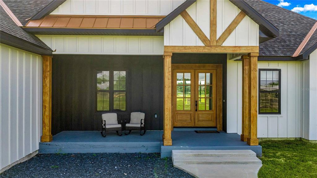 A modern farmhouse exterior features a covered porch with two chairs and wooden support columns — 9755 SE 58TH AVENUE, BELLEVIEW, FL