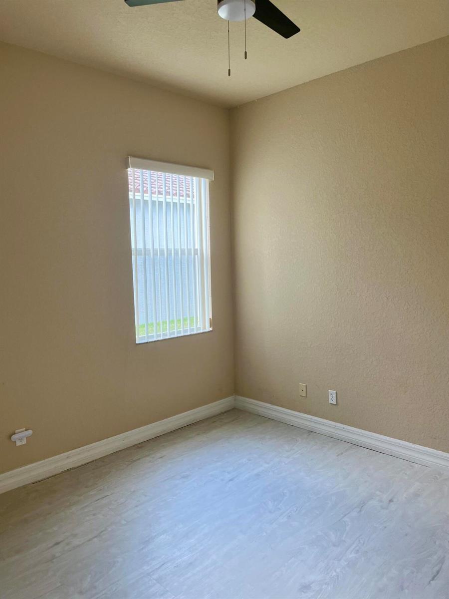 An empty bedroom features beige walls, light-colored wood-look flooring, and a vertical blind window — 5579 55th Avenue, Vero Beach FL 32967, VERO BEACH, FL