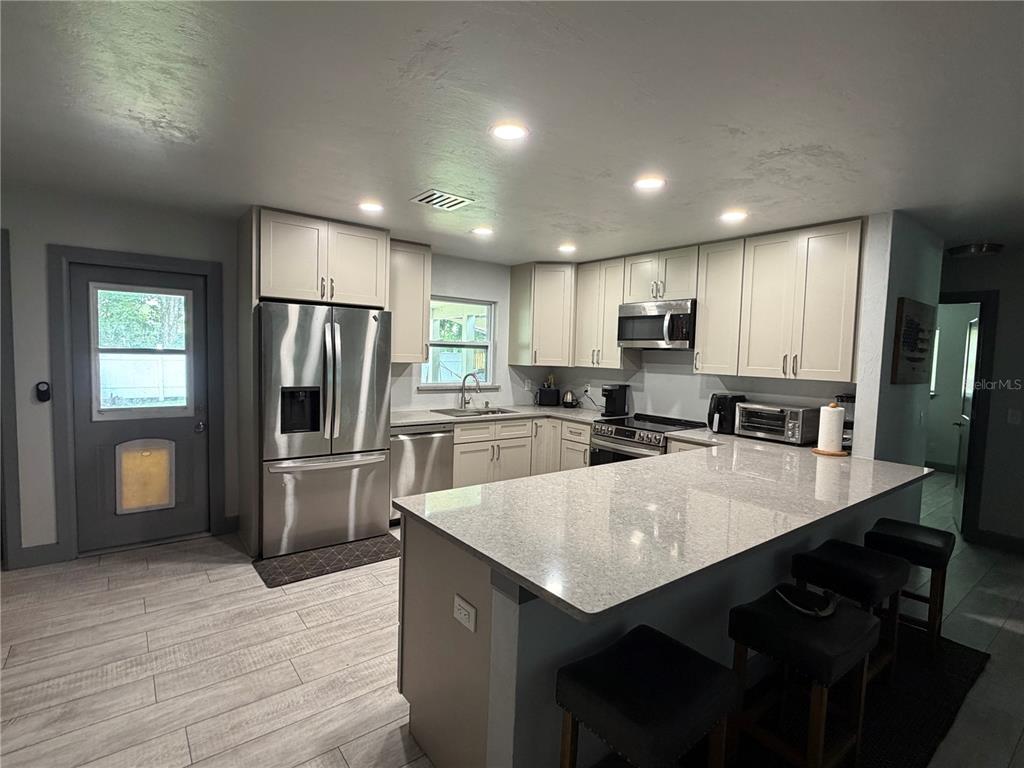 A kitchen features light-colored cabinets, stainless steel appliances, a quartz island, and tile flooring — 2436 CLAIRE AVENUE, NEW SMYRNA BEACH, FL