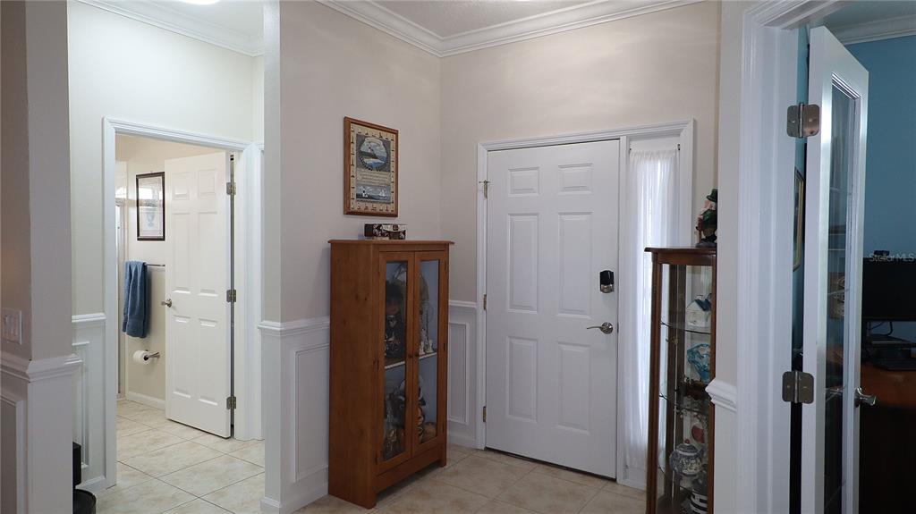 An entryway features a white front door, tile flooring, wainscoting, and two wooden display cabinets — 2293 NW 58TH TERRACE, OCALA, FL