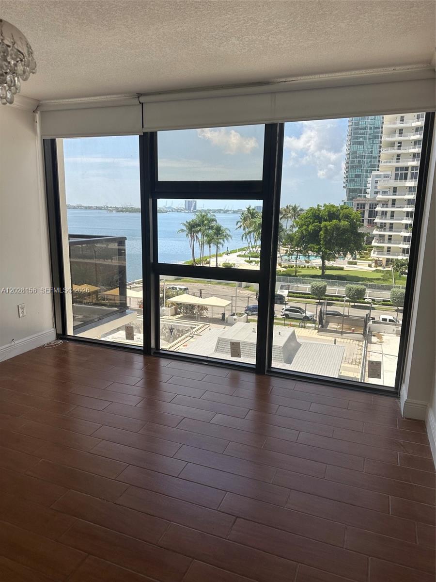 An empty room with wood-look tile flooring features large windows overlooking a bay and buildings — 600 NE 36th St # 516, Miami FL 33137, MIAMI, FL