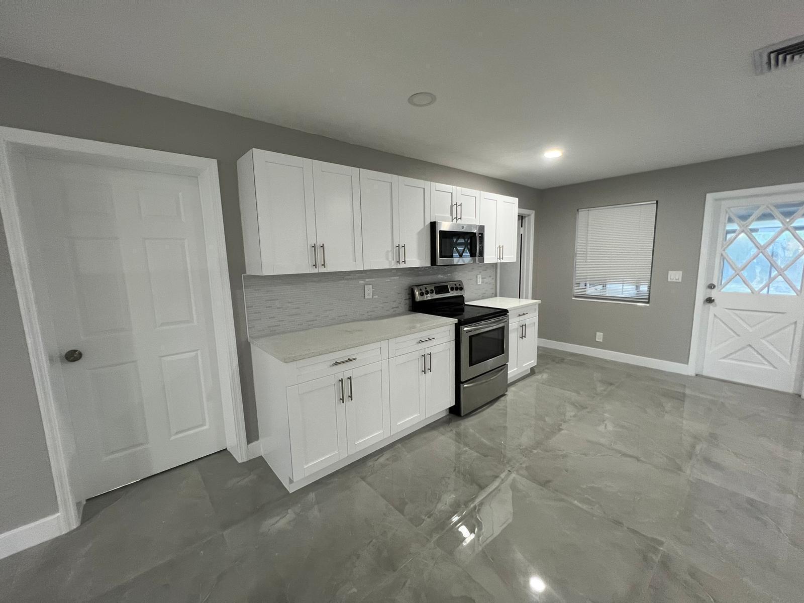 A kitchen features white cabinets, stainless steel appliances, gray tile flooring, and gray walls — 129 Euclid Boulevard, Lantana FL 33462, LANTANA, FL