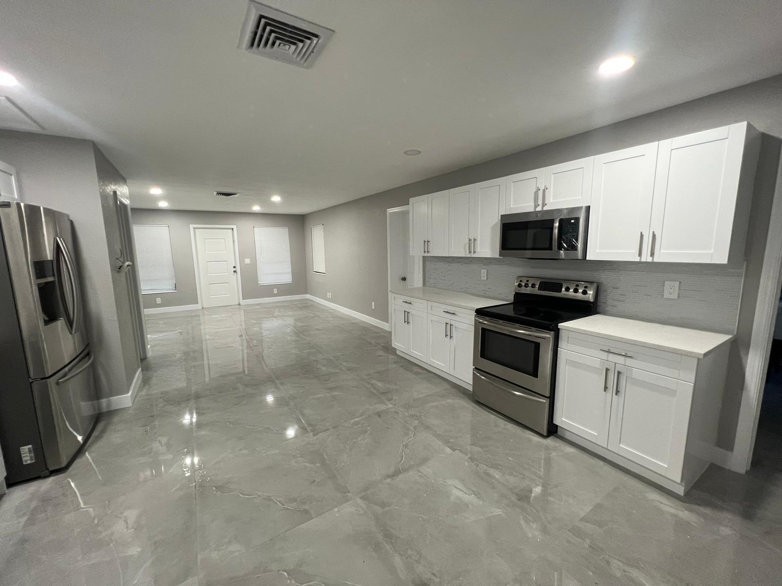 A modern kitchen with white cabinets, stainless steel appliances, and gray tile flooring — 129 Euclid Boulevard, Lantana FL 33462, LANTANA, FL