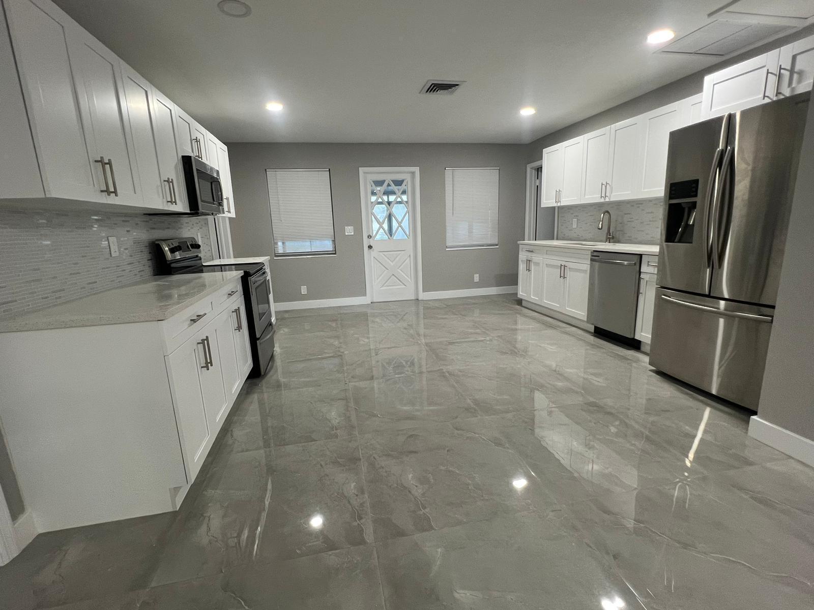 A modern kitchen features white cabinets, stainless steel appliances, and large gray tile flooring — 129 Euclid Boulevard, Lantana FL 33462, LANTANA, FL