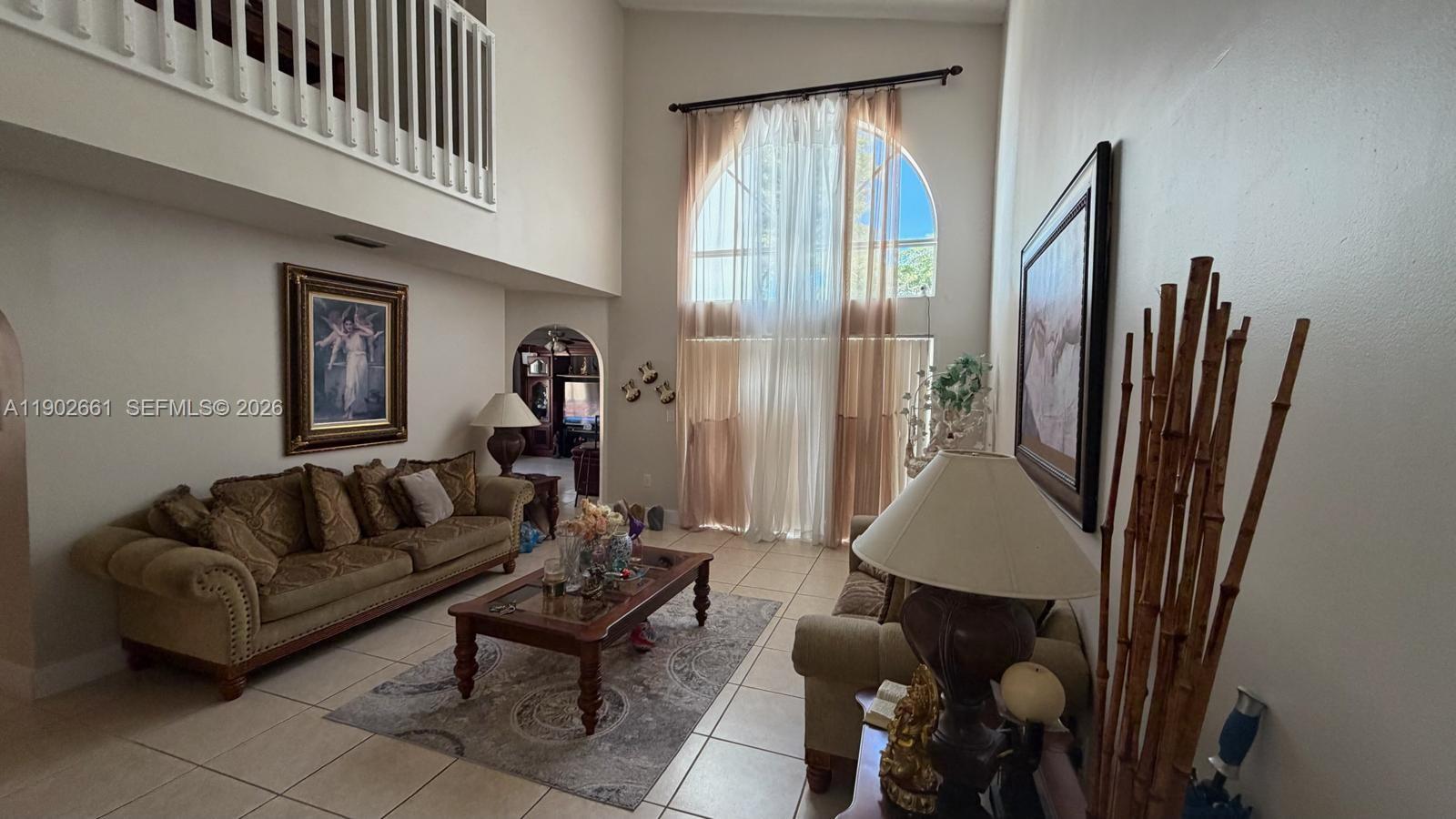 A living room features high ceilings, tile floors, a large arched window, and two sofas — 14713 SW 155th Pl, Miami FL 33196, MIAMI, FL