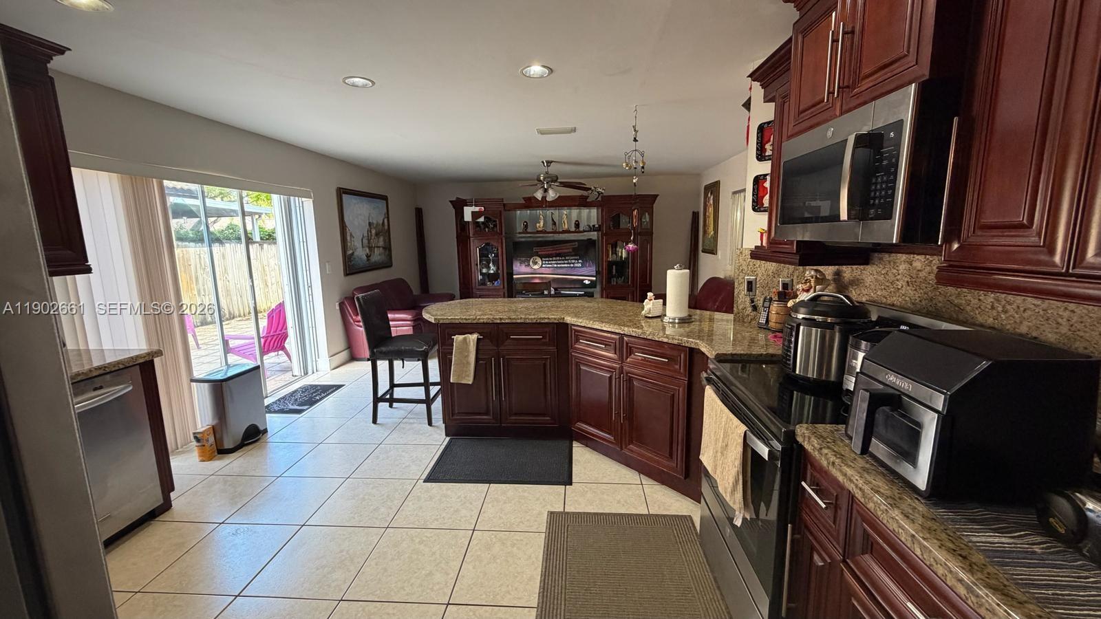 A kitchen with dark wood cabinets, granite countertops, and tile flooring opens to a living area — 14713 SW 155th Pl, Miami FL 33196, MIAMI, FL