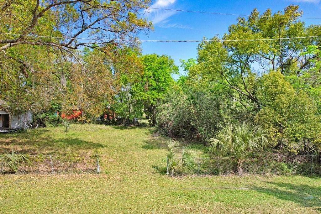 A grassy, fenced-in backyard features mature trees and a small structure on the left — 710 E OHIO STREET, PLANT CITY, FL