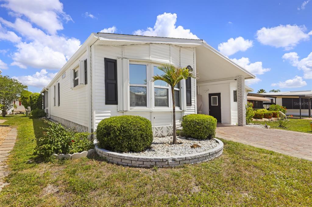 A white manufactured home features a brick-paved driveway, a small palm tree, and landscaping — 2100 KINGS HIGHWAY UNIT 744, PORT CHARLOTTE, FL