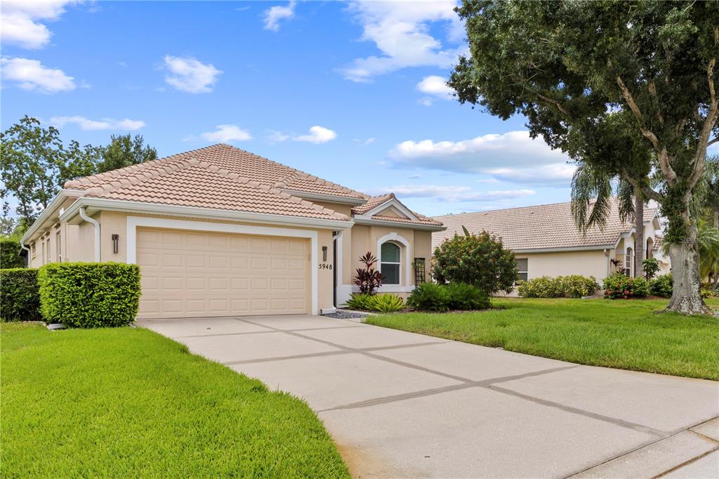 A single-story house with a beige stucco exterior, a tile roof, and a concrete driveway — 5948 SANDSTONE AVENUE, SARASOTA, FL