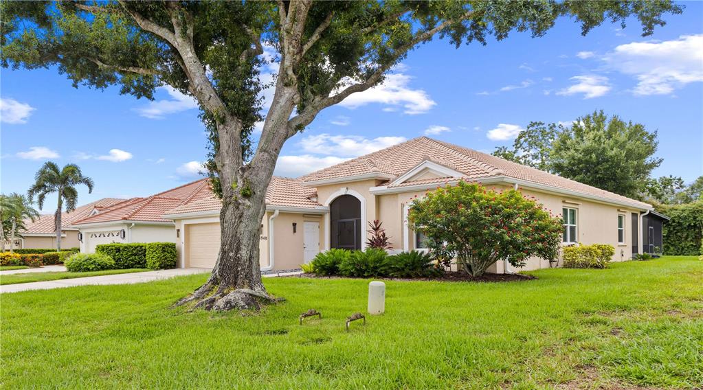 A single-story house with a tile roof, beige stucco exterior, and a large front tree — 5948 SANDSTONE AVENUE, SARASOTA, FL