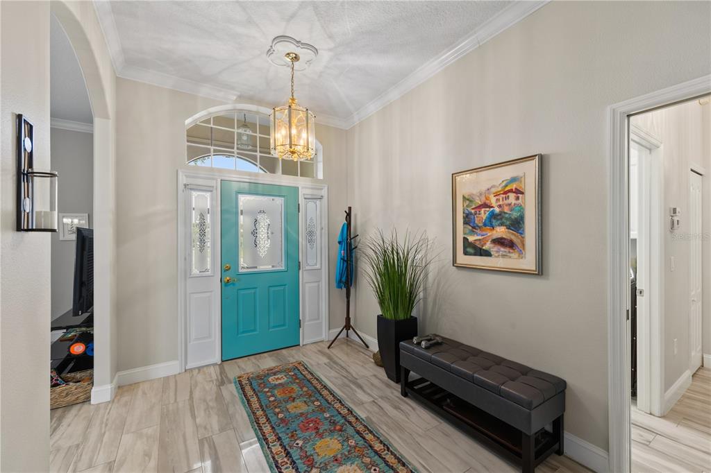 A bright entryway features a teal front door, tile flooring, a bench, and a chandelier — 5948 SANDSTONE AVENUE, SARASOTA, FL
