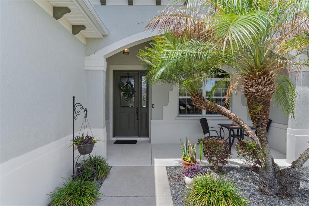A front entryway features a gray door, a concrete walkway, and a small palm tree — 2254 ISLEWORTH CIRCLE, THE VILLAGES, FL