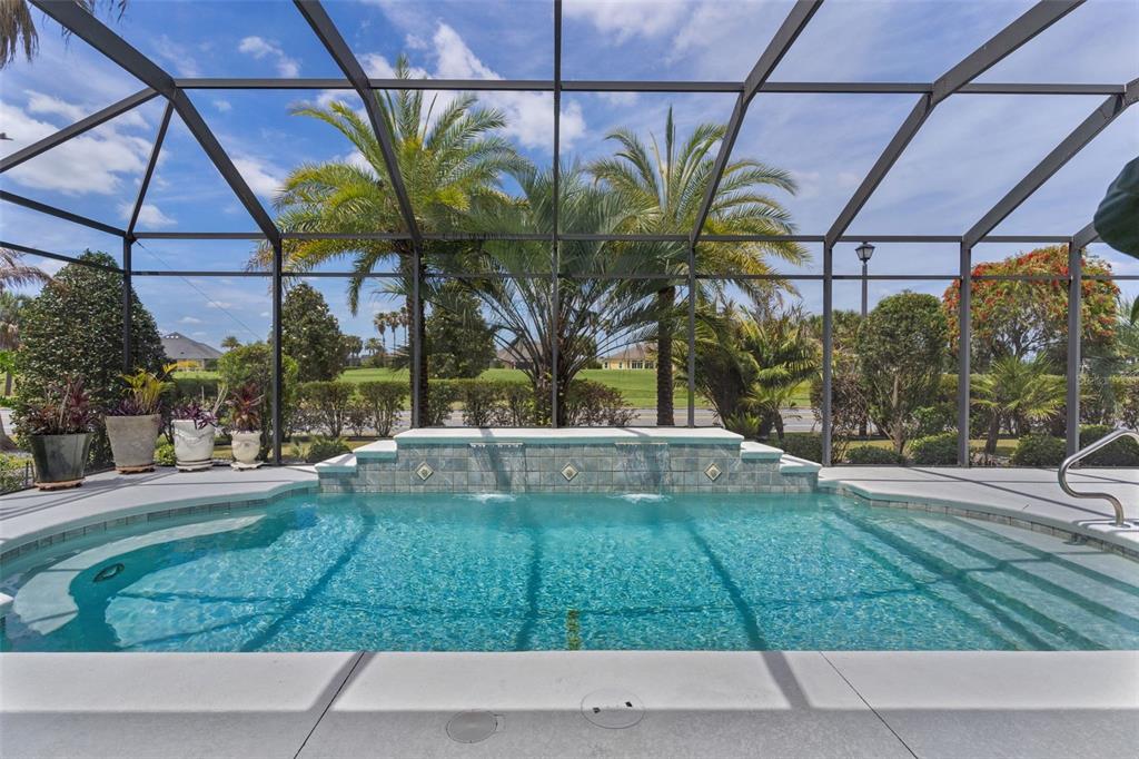 A screened-in swimming pool with a tiled water feature and palm trees in the background — 2254 ISLEWORTH CIRCLE, THE VILLAGES, FL