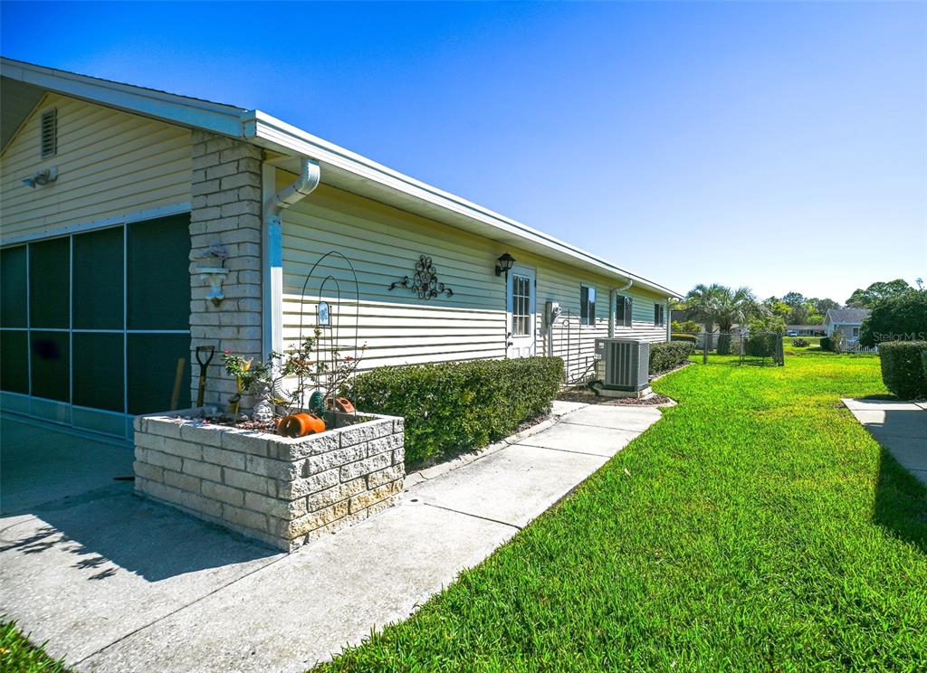 A side view of a house with light yellow siding, a brick planter, and a sidewalk — 11055 SW 77TH COURT, OCALA, FL