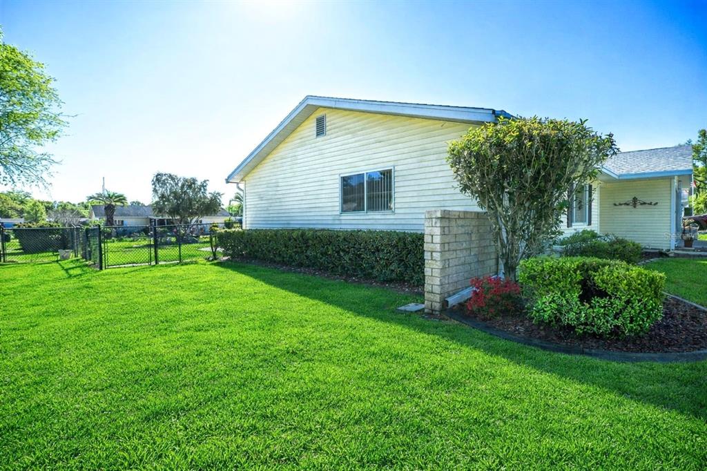 A side view of a yellow house with a brick wall and a green lawn — 11055 SW 77TH COURT, OCALA, FL