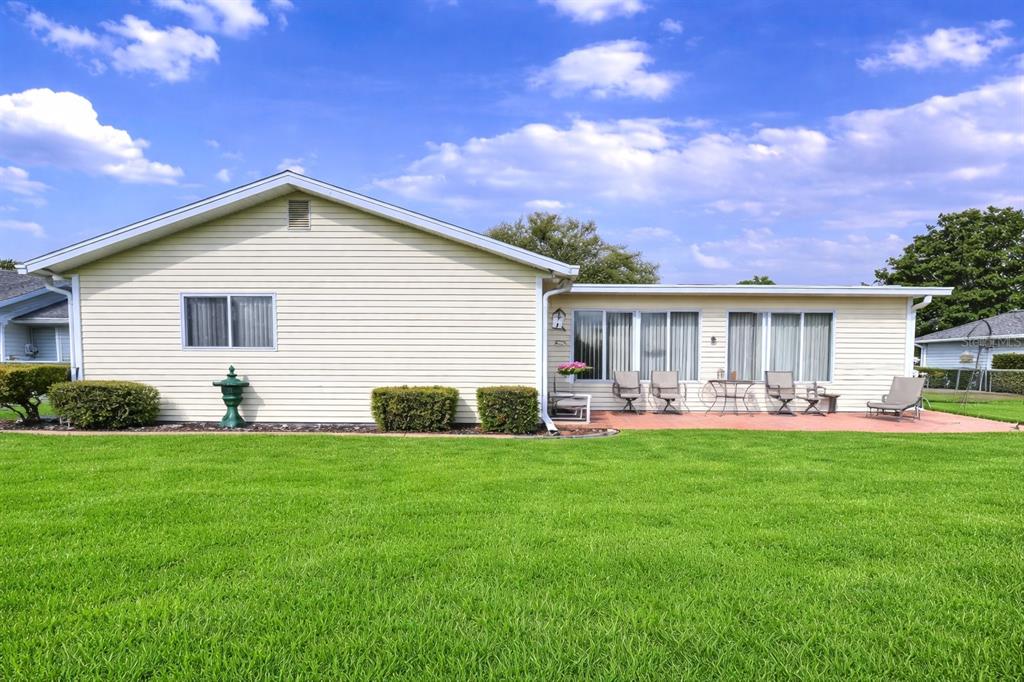The exterior of a light-colored house features a large lawn and a paved patio area — 11055 SW 77TH COURT, OCALA, FL