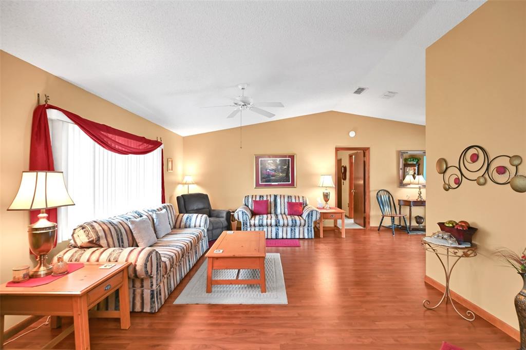 A living room features striped sofas, wood-look flooring, a vaulted ceiling, and a ceiling fan — 11055 SW 77TH COURT, OCALA, FL