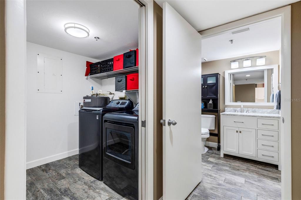 A laundry room with black appliances and shelving sits adjacent to a white bathroom vanity — 3980 IRONWOOD CIRCLE UNIT 404, BRADENTON, FL