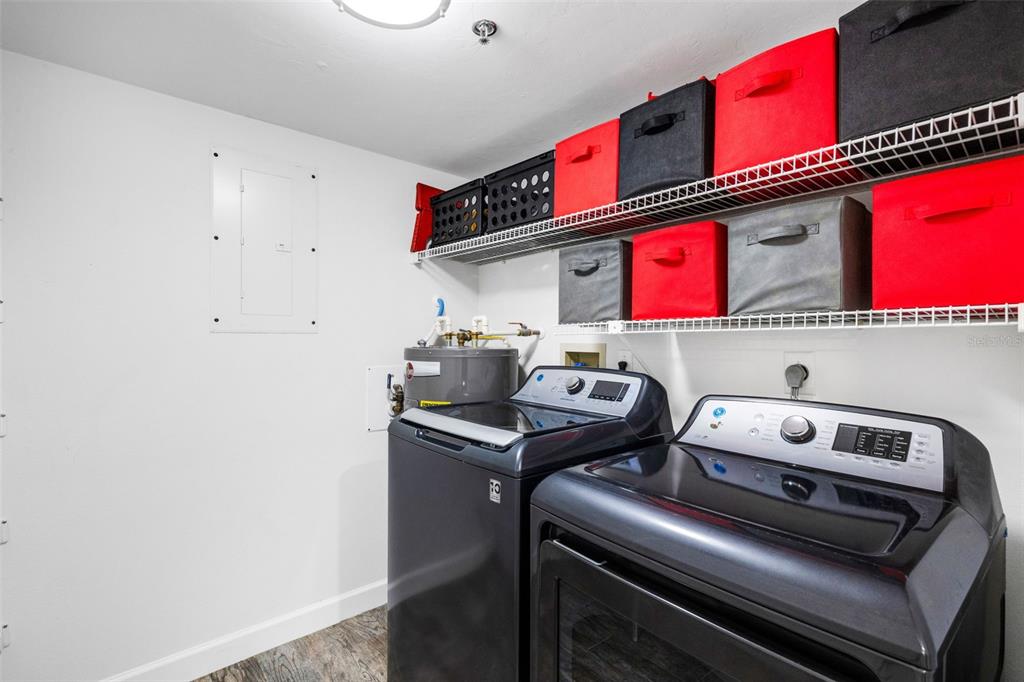 A laundry room features dark appliances, a water heater, and wire shelving with storage bins — 3980 IRONWOOD CIRCLE UNIT 404, BRADENTON, FL