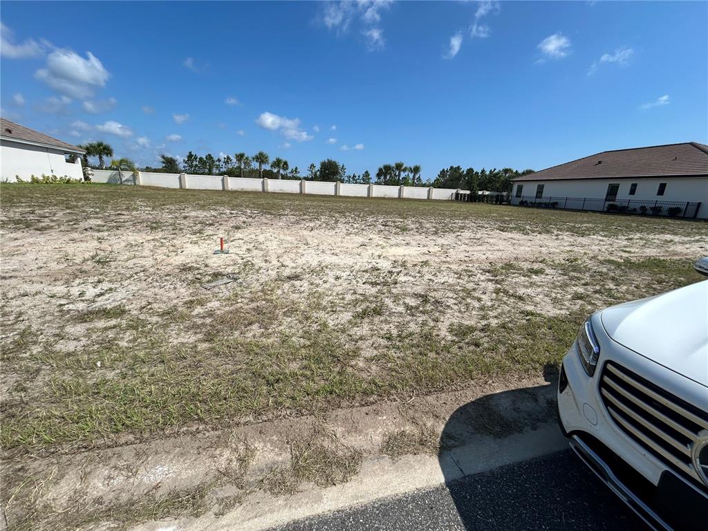 A vacant residential lot with sandy ground sits between two houses under a blue sky — 24 DEL PALMA DRIVE, PALM COAST, FL