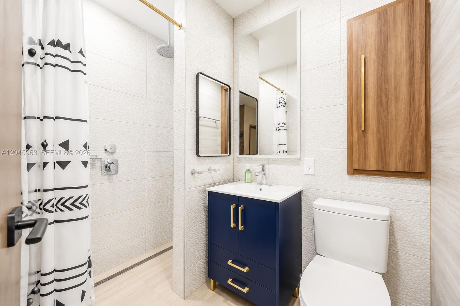A bathroom features a blue vanity, a walk-in shower, and a toilet against tiled walls — 14888 SW 140th St # 1, Miami FL 33196, MIAMI, FL